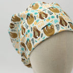 Side view of sloth-patterned scrub cap showing brown sloths with teal and orange tropical foliage design