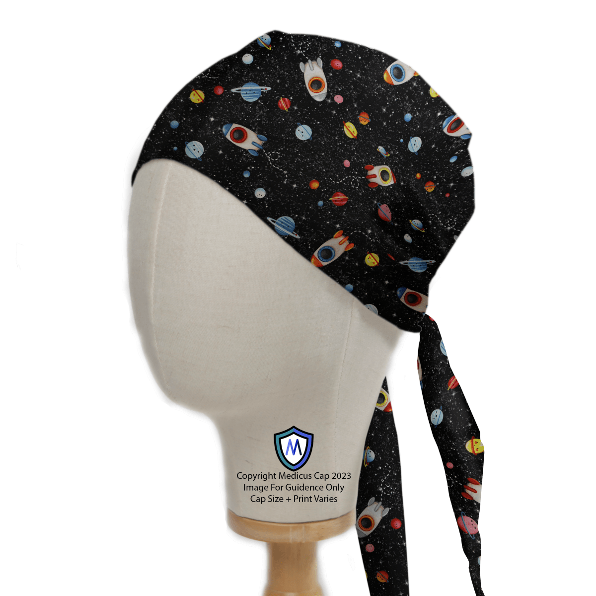 A mannequin head displays the Spaceships Planets Rockets Scrub Cap by Medicus Scrub Caps, featuring a vibrant space-themed pattern with spaceships, planets, and rockets. The black cap has long ties at the back and a logo and text at the bottom.