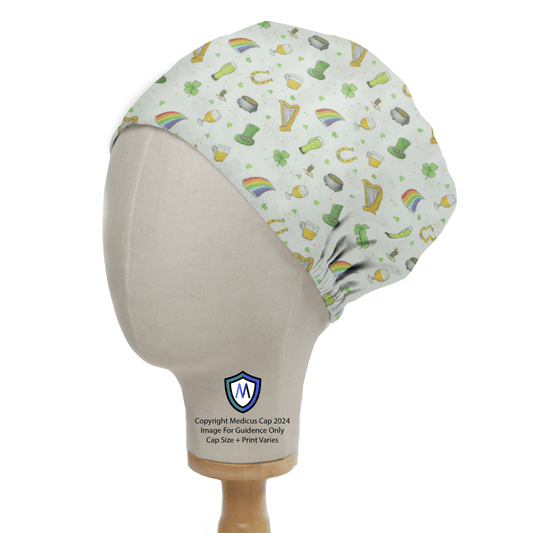 A mannequin head displays the Medicus Scrub Caps St Patricks Day Trinkets Scrub Cap, featuring a festive pattern of shamrocks, rainbows, leprechaun hats, and gold coins on a light background with vibrant illustrations.