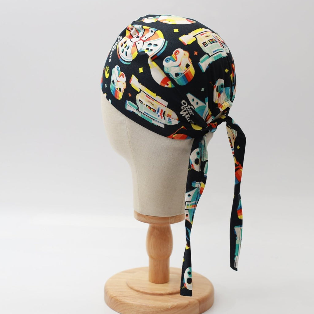 The mannequin wears a Medicus Scrub Caps Star Wars Pride Spaceships Scrub Cap, featuring colorful spaceships on a black background. The cap ties at the back.