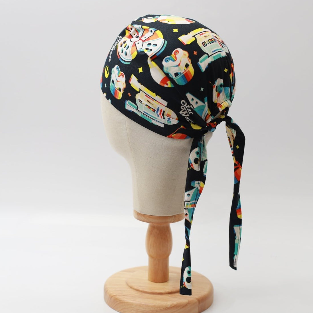 The mannequin wears a Medicus Scrub Caps Star Wars Pride Spaceships Scrub Cap, featuring colorful spaceships on a black background. The cap ties at the back.