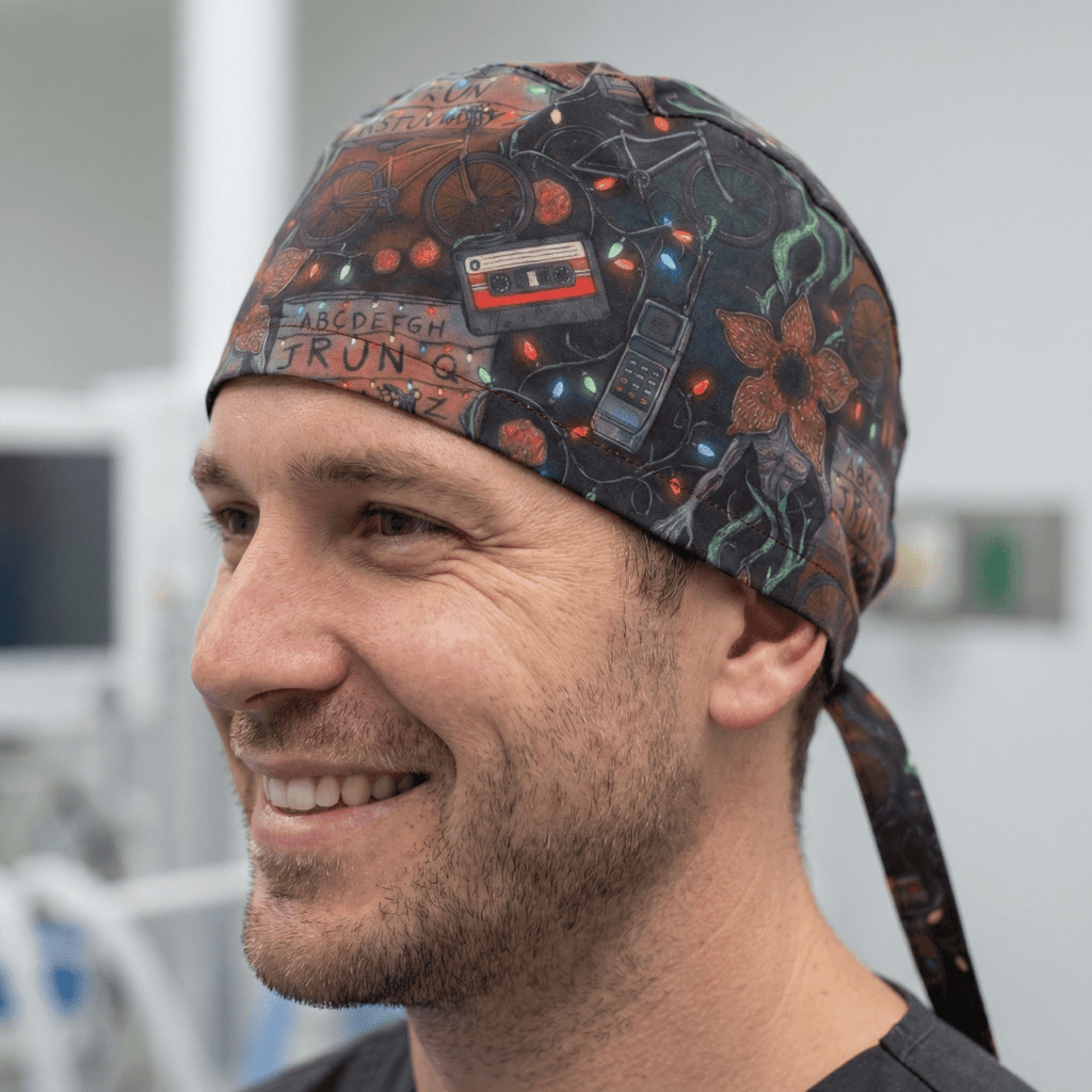 Side profile view of dark scrub cap featuring retro icons, cassette tapes, and floral patterns in orange and teal