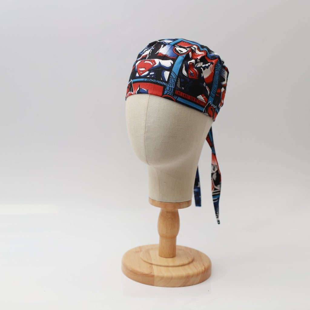Mannequin head wearing Medicus Scrub Cap with Superman vs Batman #2 print, on a wooden stand against a white backdrop.