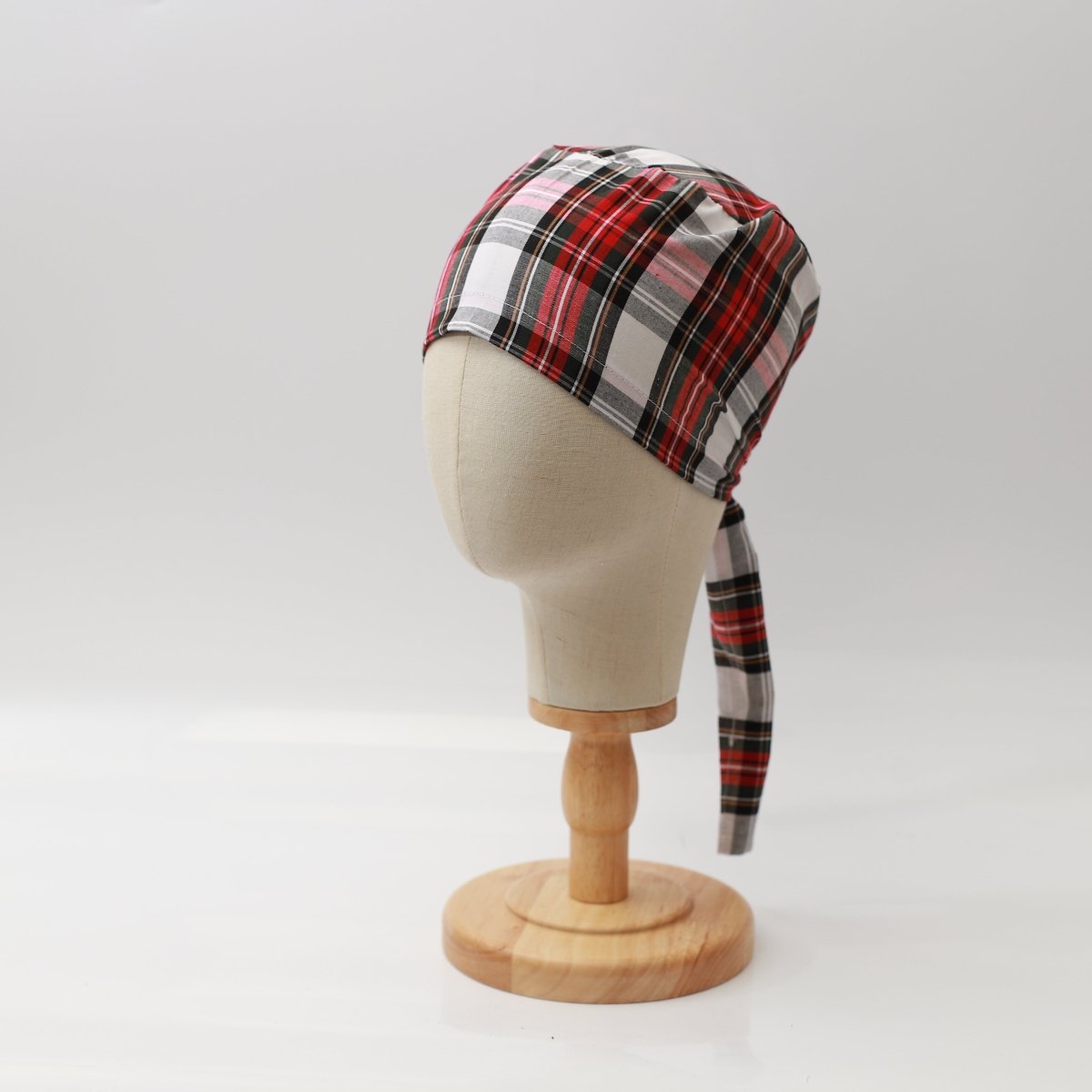 Mannequin head wearing Medicus Scrub Cap with red and white plaid pattern, on a wooden stand against a white backdrop.