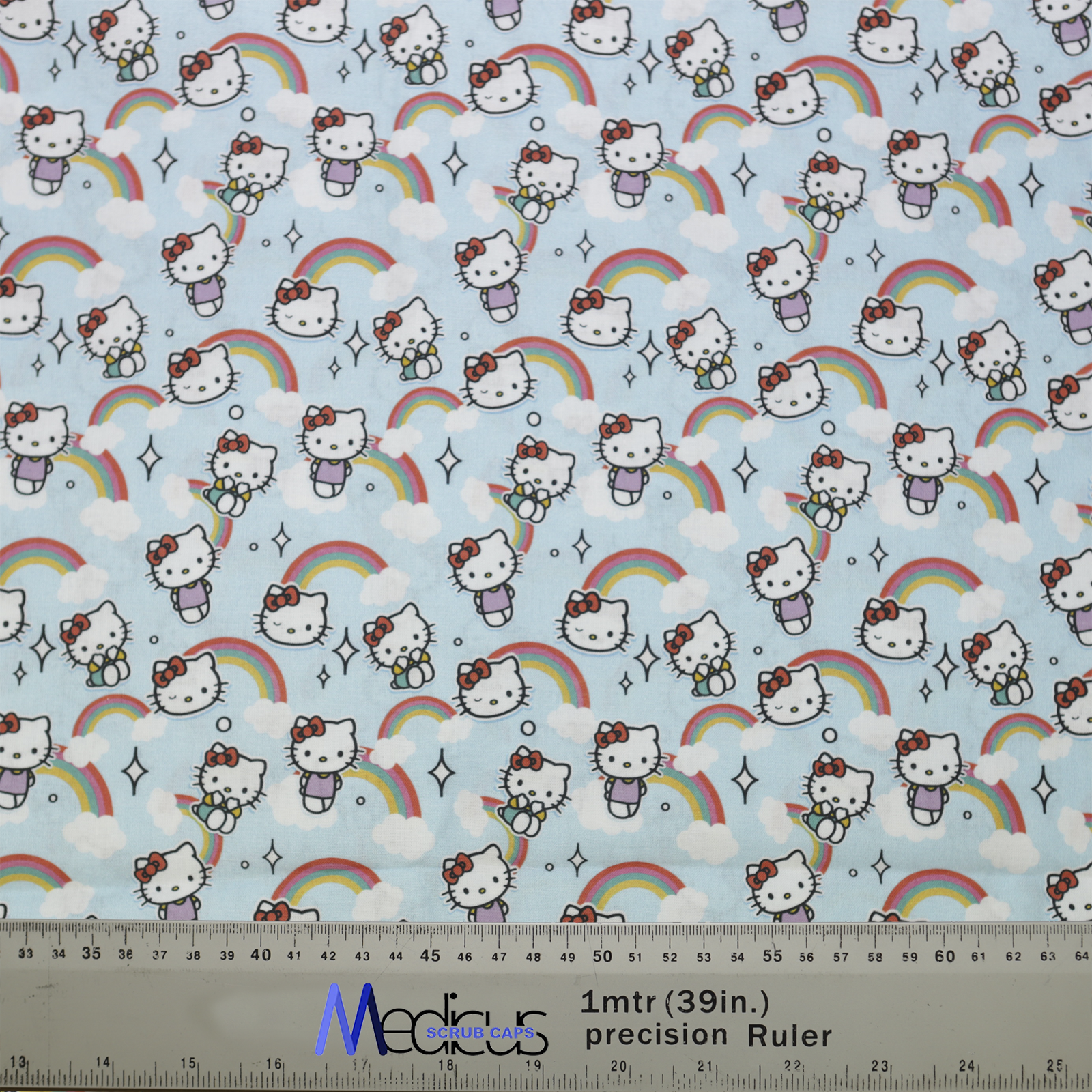 The Medicus Scrub Caps Hello Kitty Scrub Cap features a light blue fabric with Hello Kitty, rainbows, clouds, and stars, alongside a precision ruler for sizing.