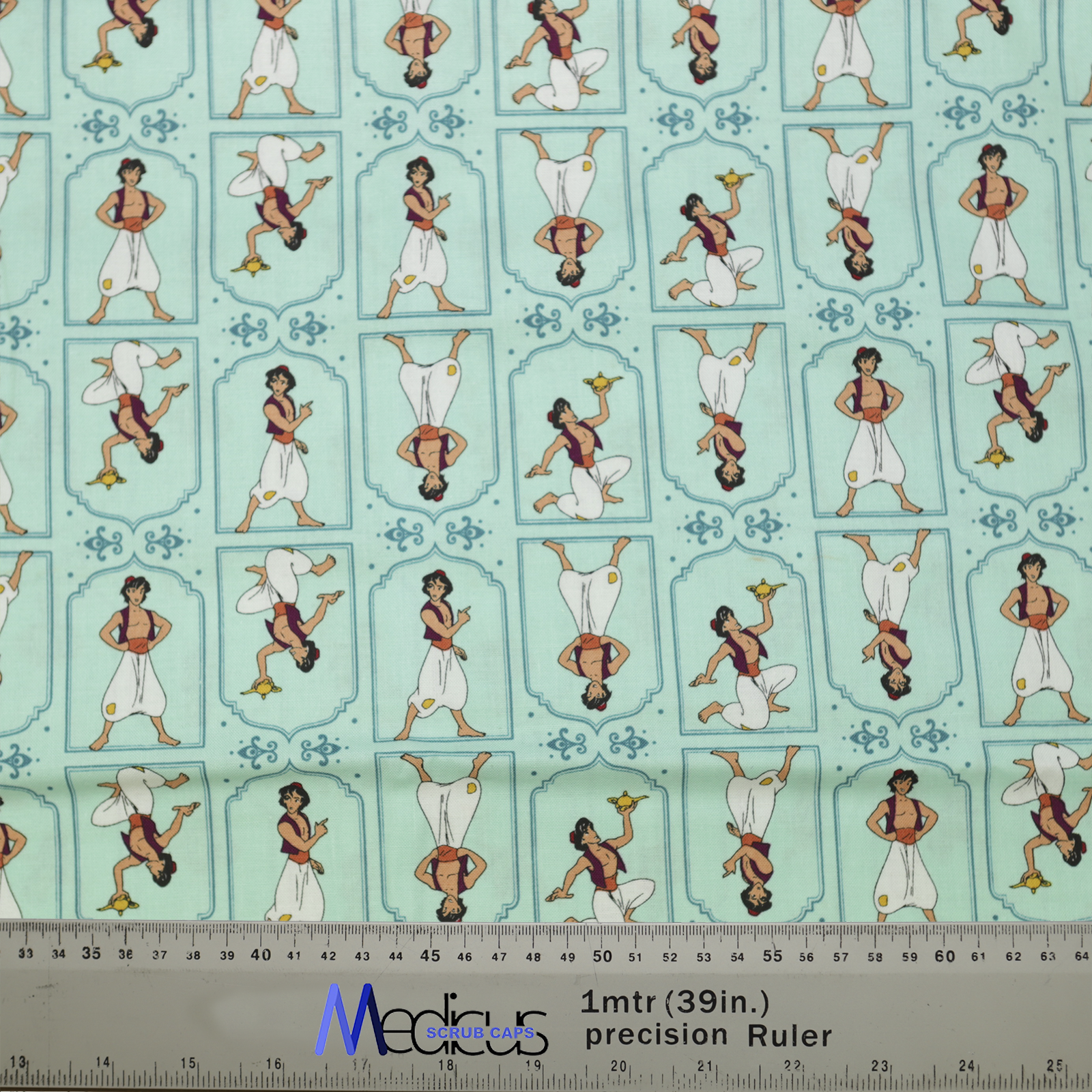 The Disney Aladdin Pose Theatre Cap by Medicus Scrub Caps features light blue fabric with playful Aladdin poses, perfect for whimsical, comfortable scrub caps. Ruler included for scale.