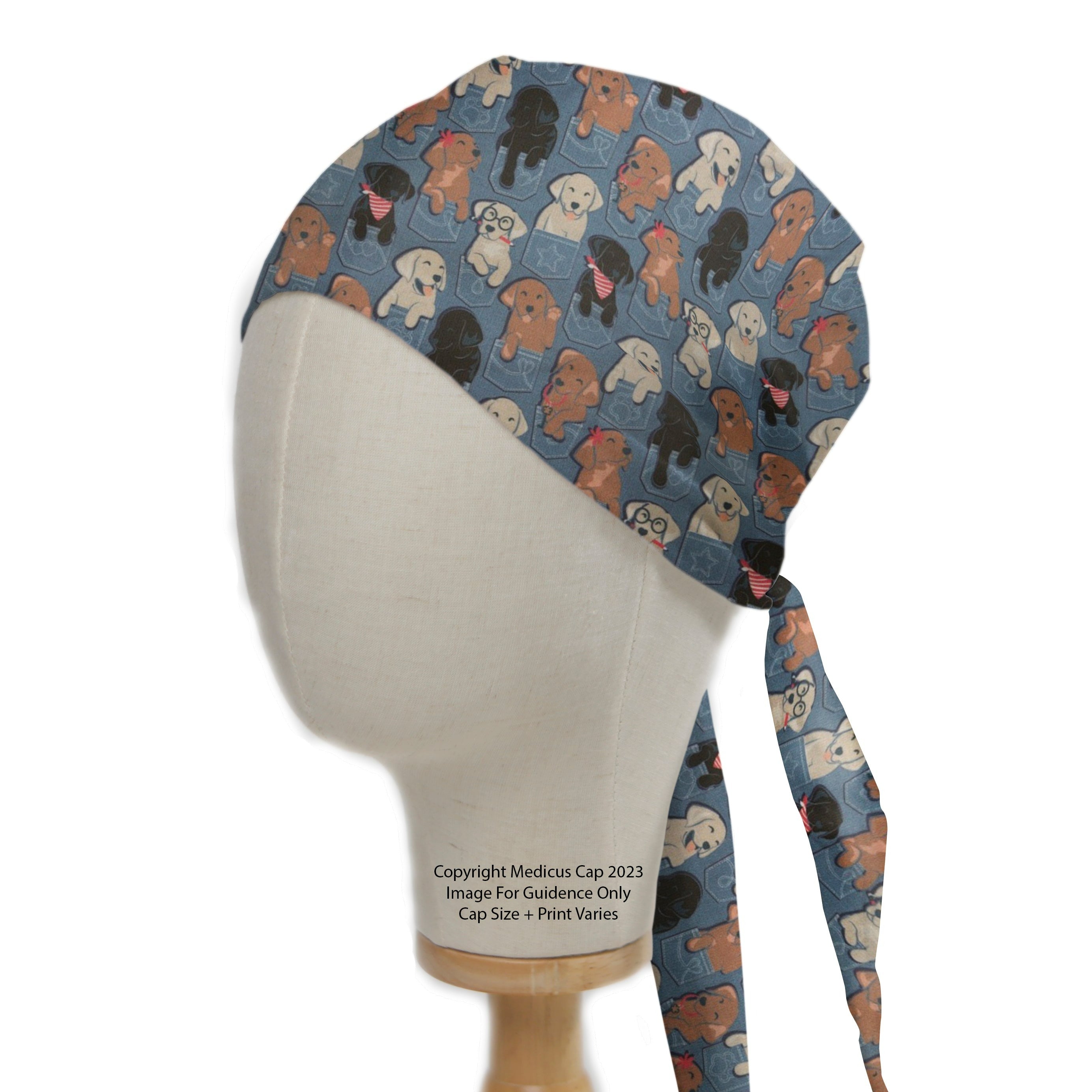 A mannequin head displays a Medicus Scrub Cap featuring playful dogs in jean pockets. The "Dogs In Jean Pockets Scrub Cap" includes two long ties at the back.