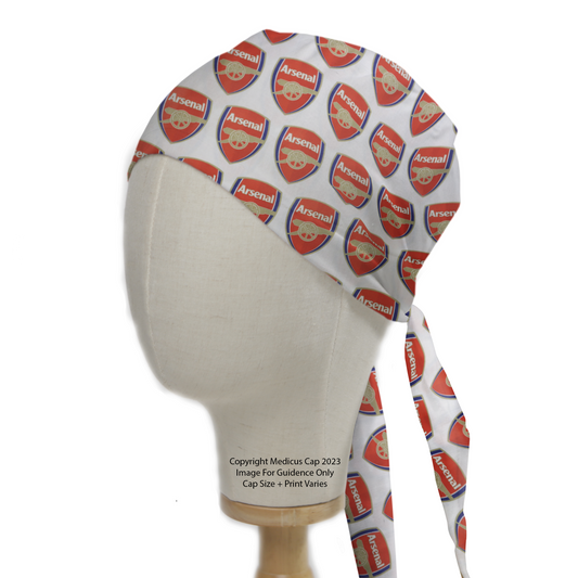 A mannequin head wears a Football Club Arsenal Scrub Cap by Medicus Scrub Caps, featuring red and white Arsenal logos with a tie-back design for adjustability.