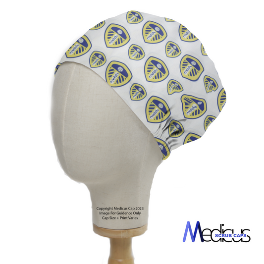 The white Medicus Scrub Cap features a blue and yellow Leeds United shield pattern, crafted for medical professionals and displayed on a mannequin head.