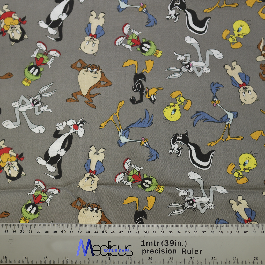 Medicus Scrub Caps fabric featuring Looney Tunes characters on grey, including Bugs Bunny, Taz, and Tweety. Ruler at bottom shows scale.