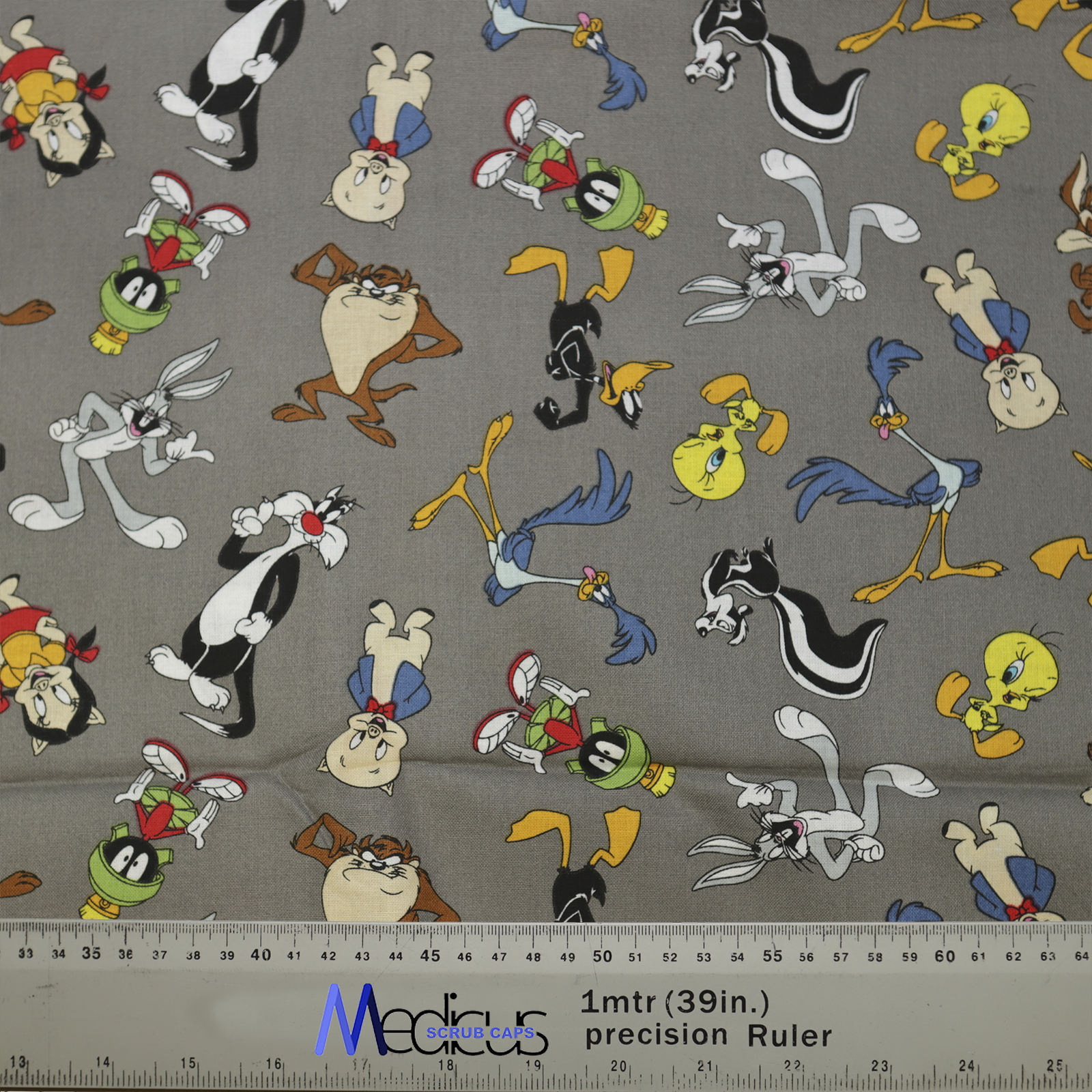 Medicus Scrub Caps fabric featuring Looney Tunes characters on grey, including Bugs Bunny, Taz, and Tweety. Ruler at bottom shows scale.