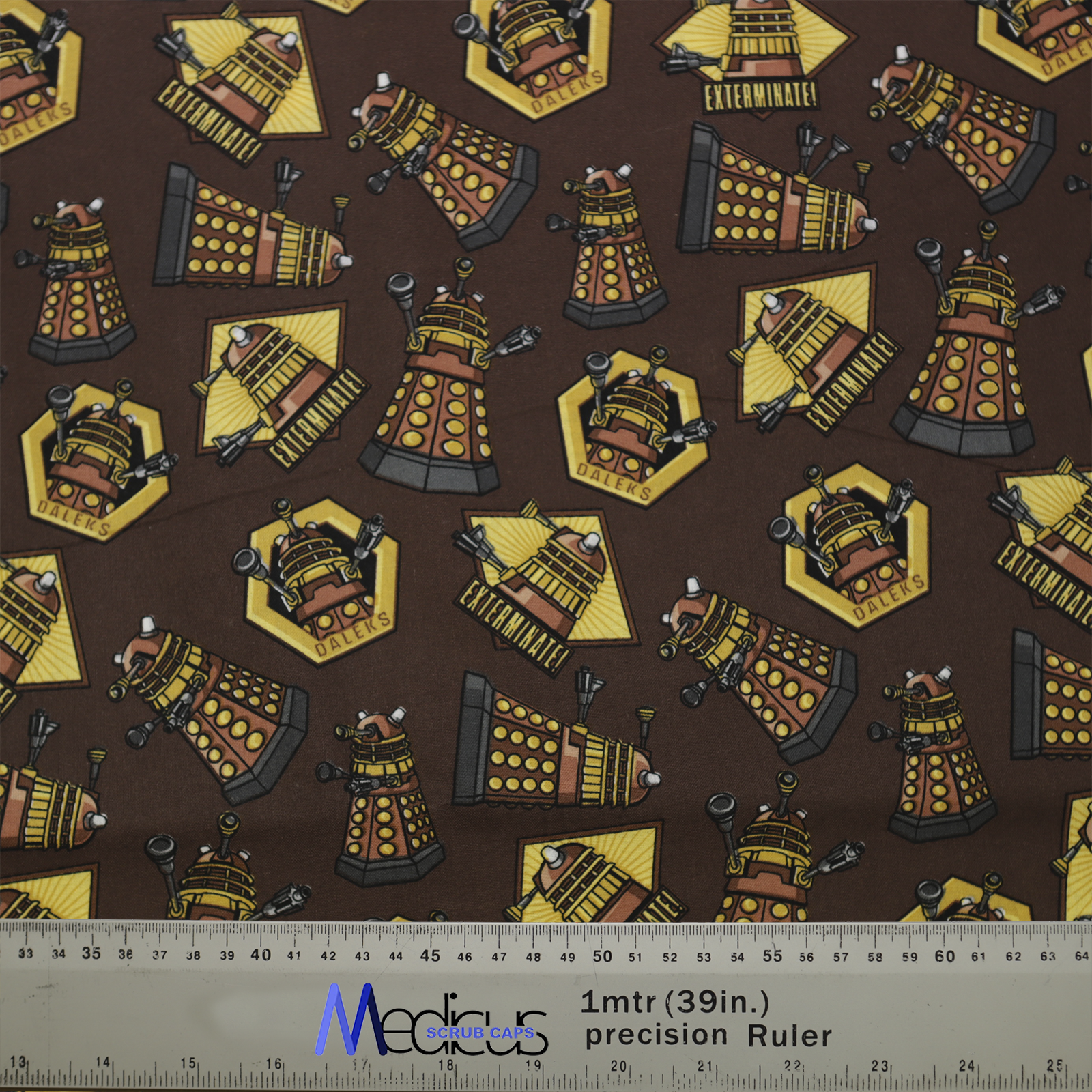 The Dr Who Dalek Brown Scrub Cap by Medicus Scrub Caps features Dalek designs on a brown background with hexagonal motifs. Includes a 1m (39in) ruler.