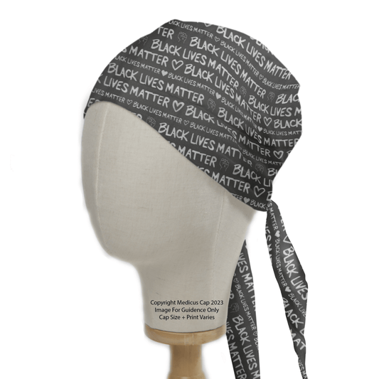 A mannequin head presents a Black Lives Matter BLM scrub cap, featuring BLACK LIVES MATTER with white text and hearts, highlighting inclusivity. Ideal for healthcare workers, it ties at the back. © Medicus Scrub Caps 2023. Image is for reference; cap size and print may vary.