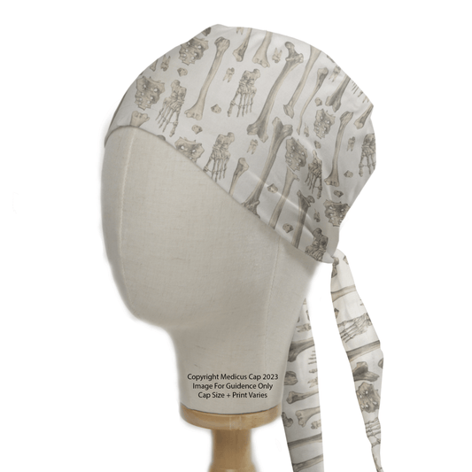 A mannequin head displays the Medicus Scrub Caps Bones Scrub Cap, featuring a medical-themed pattern of bones and joints. This white healthcare essential has long ties at the back and is on a wooden stand, highlighting its sustainable design.