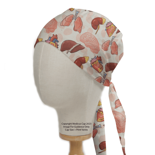 A mannequin head displays the Medicus Scrub Caps Brain Heart Kidney Liver scrub cap, featuring anatomical prints like the heart and liver. Crafted from hypoallergenic 100% cotton, it ensures comfort with style. The off-white background enhances its medical theme, complete with tie straps at the back.