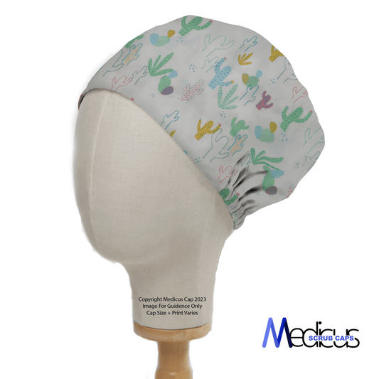 A mannequin head displays the eco-friendly Cactus Abstract Desert Scrub Cap by Medicus Scrub Caps, featuring a vibrant design of gray with green, yellow, pink, and blue cacti. The brands logo is located at the bottom right.