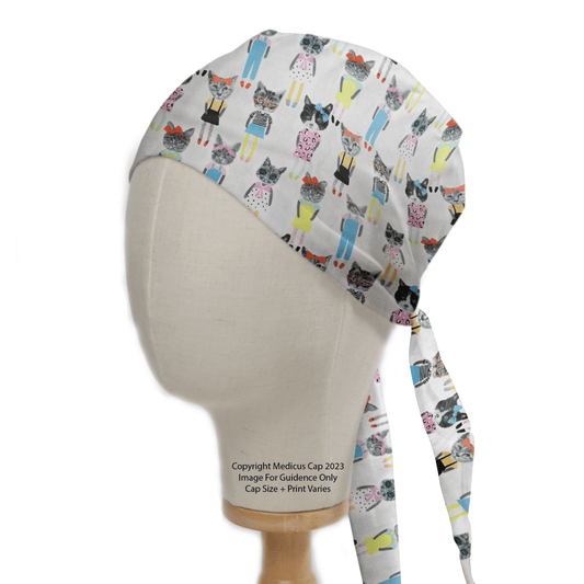 A mannequin head displays the Medicus Scrub Caps Cat Cartoon Dress Up Scrub Cap, eco-friendly with vibrant cat designs on white. It showcases cats in diverse outfits and poses and includes back ties for a secure fit.