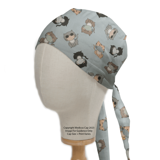 A mannequin head displays a Medicus Scrub Caps light blue Cat Face Masks scrub cap featuring playful cartoon cats and ties at the back. Bottom text reads, Copyright Medicus Cap 2023. Image for guidance only. Cap size and print vary.