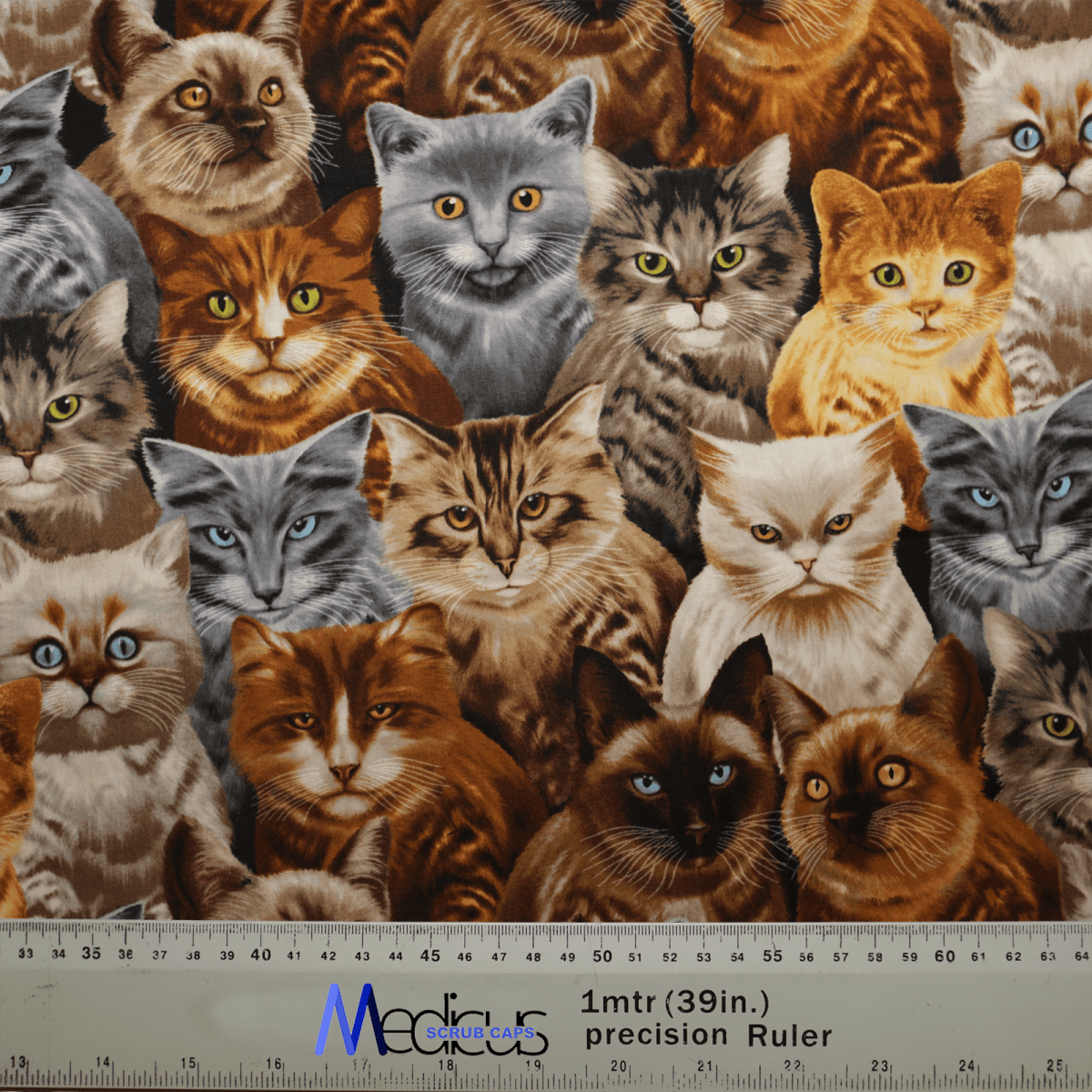 Medicus Scrub Caps Cat Starring Scrub Cap boasts a vibrant fabric pattern of cat faces in brown, gray, and orange. It includes inclusive designs and a ruler for inch and centimeter measurements, fusing style with eco-friendly practicality.