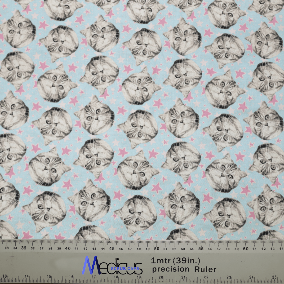 Discover Medicus Scrub Caps new Cat Stars design, boasting cute cat faces with large eyes on a light blue background with pink stars. This eco-friendly, reusable scrub cap includes a ruler for scale and adds a playful flair to your work attire.