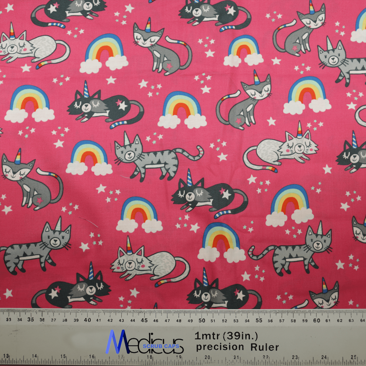 The Cats Unicorn Rainbow Pink Scrub Cap by Medicus Scrub Caps features a pink background with playful gray cats, unicorn rainbows, stars, and clouds. Its comfortable, breathable, and sustainable. A ruler at the bottom shows measurements in inches and meters for scale.