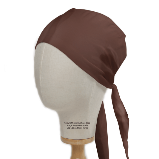 A mannequin head displays the Classic Plain Brunette Brown Scrub Cap by Medicus Scrub Caps, featuring a smooth, shiny satin-like fabric with a knot at the back. The mannequin resembles one from a theatre hat display and is set on a simple wooden stand.