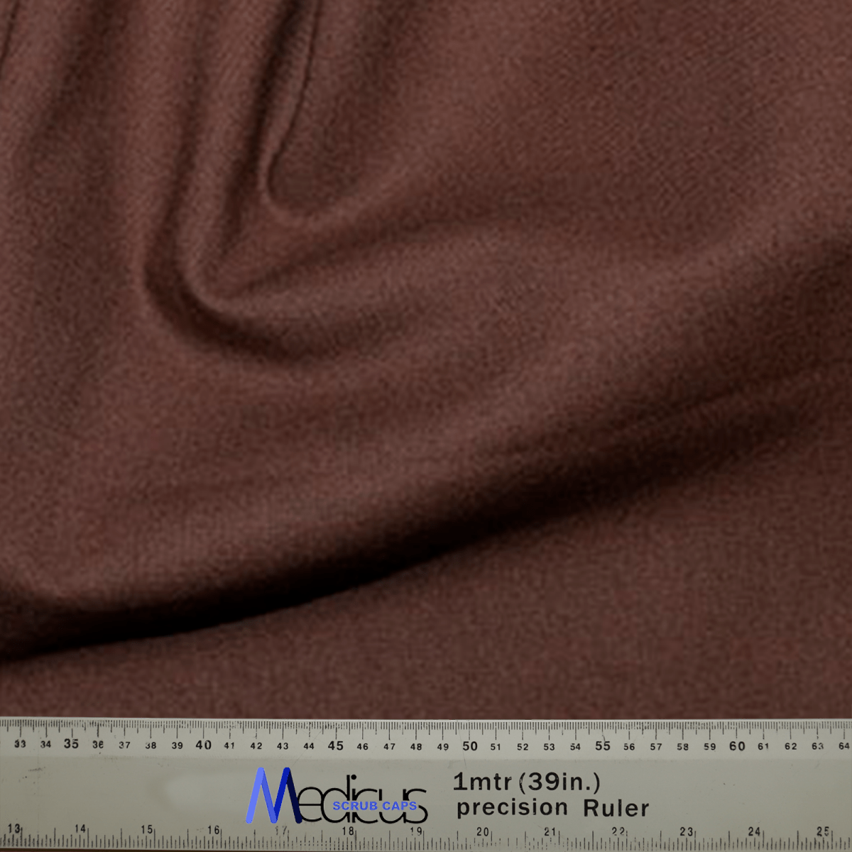 A close-up of soft, sustainable brown fabric draped in folds, paired with a precision ruler showing measurements in cm and inches—perfect for crafting the Classic Plain Brunette Brown Scrub Cap by Medicus Scrub Caps for medical professionals.