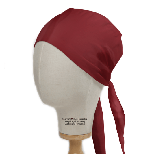 A mannequin head features the Classic Plain Claret Red Scrub Cap by Medicus Scrub Caps, tied at the back with ribbon-like ends. Designed for durability, this smooth theatre hat is perfect for medical or kitchen use.