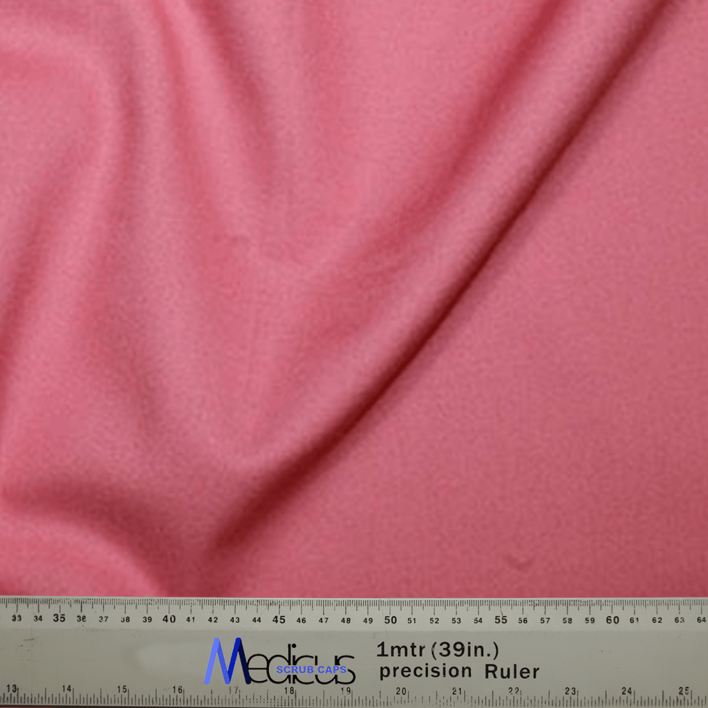 A close-up showcases the coral pink fabric of a Classic Plain Scrub Cap by Medicus Scrub Caps draped over a 39-inch ruler. The soft, textured material accompanies a silver Media precision ruler with blue and black text, assuring unmatched durability.