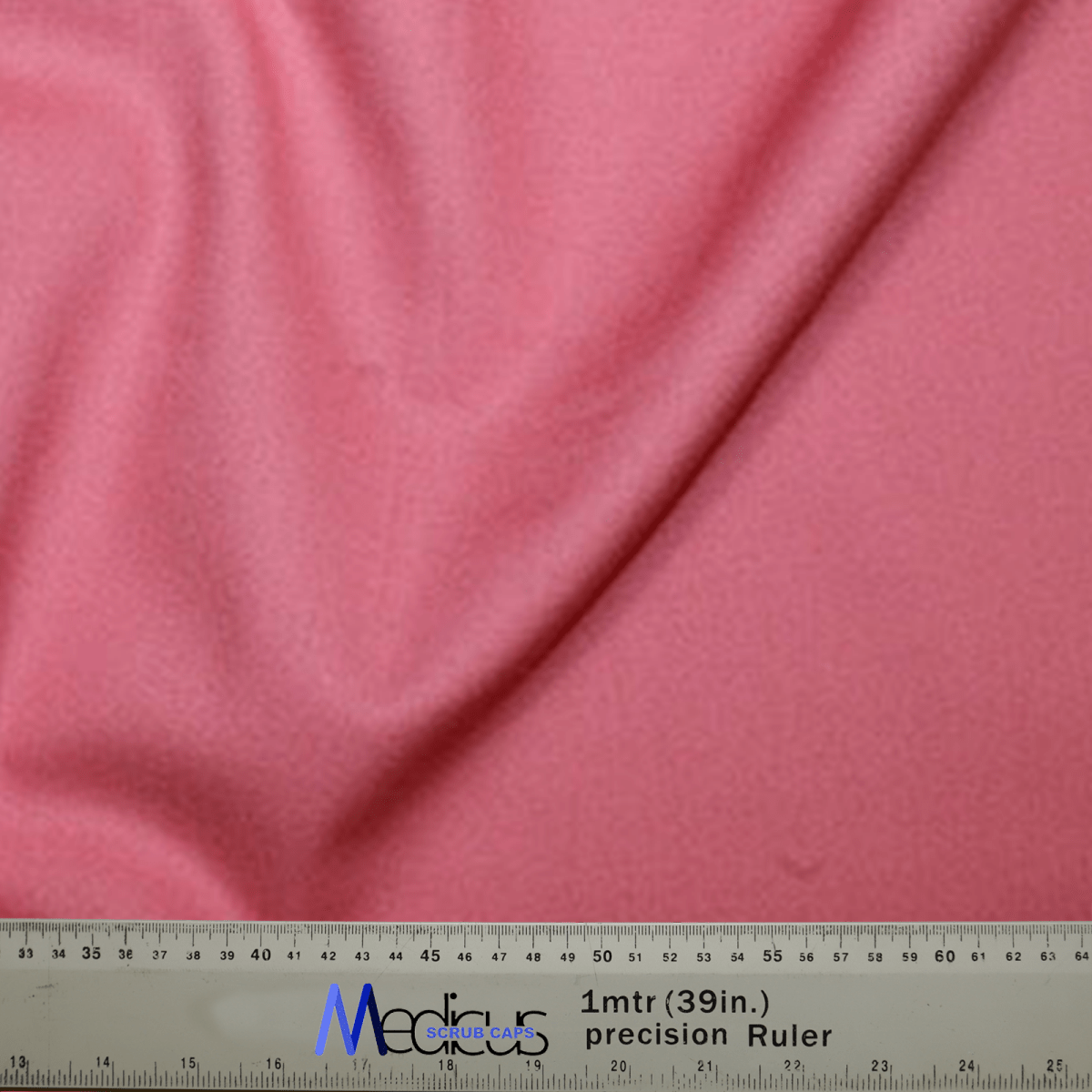A close-up showcases the coral pink fabric of a Classic Plain Scrub Cap by Medicus Scrub Caps draped over a 39-inch ruler. The soft, textured material accompanies a silver Media precision ruler with blue and black text, assuring unmatched durability.