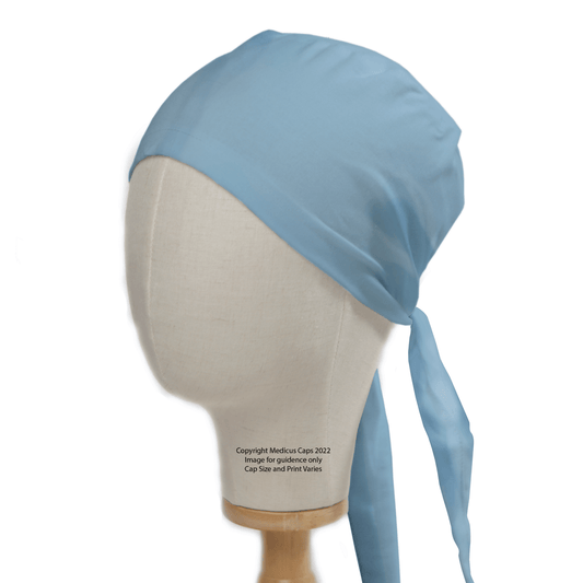 A mannequin head displays a durable Classic Plain Cyan Blue Scrub Cap by Medicus Scrub Caps, featuring ties draping down the back, all set on a wooden stand against a white backdrop.