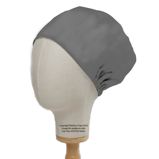 A mannequin head displays the Classic Plain Dark Grey Scrub Cap by Medicus Scrub Caps, elegantly covering the entire head and gathering slightly at the back. It sits gracefully on a simple wooden stand against a plain white backdrop.