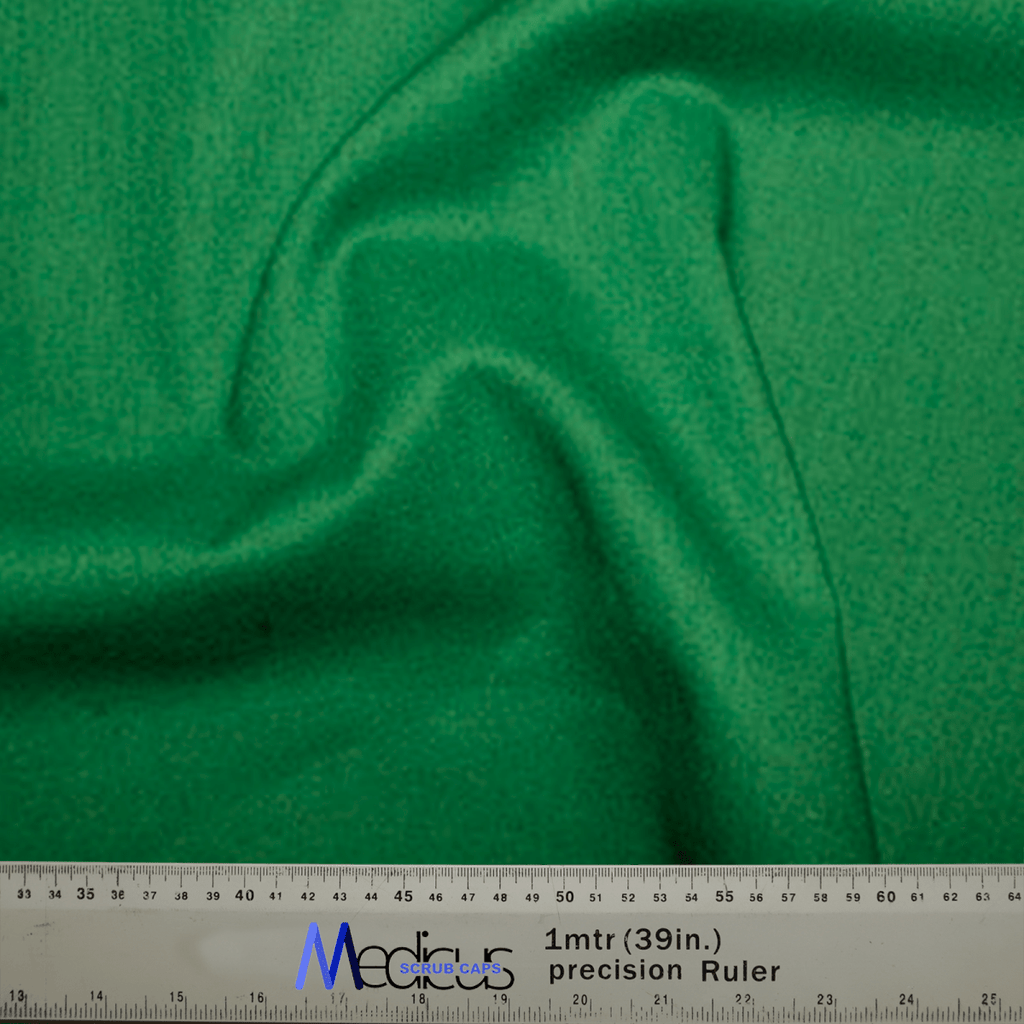 A close-up of Classic Plain Fir Green Scrub Cap fabric by Medicus Scrub Caps shows a gentle fold in the center. A ruler at the bottom measures its width in inches and centimeters, displaying a 1-meter segment with branding text, ideal for healthcare professionals estimating fittings.