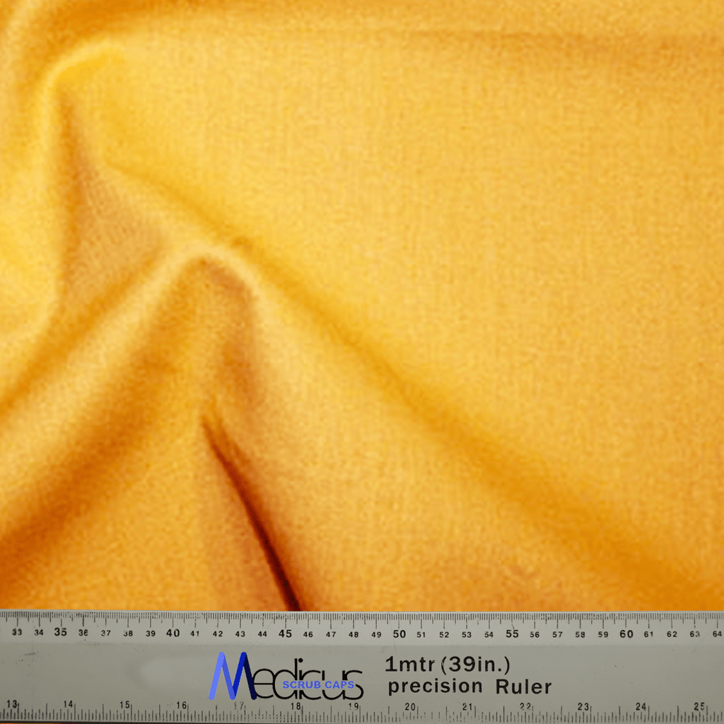 A Classic Plain Gold Yellow Scrub Cap from Medicus Scrub Caps drapes over a precise Medicare ruler, featuring durable design with clear measurements in centimeters and inches.