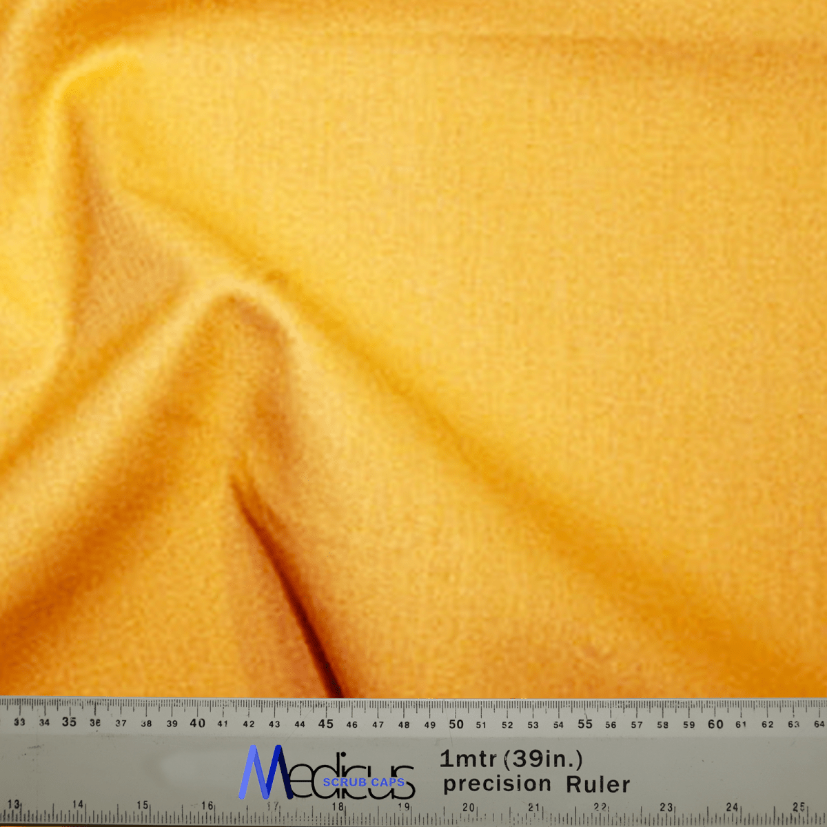 A Classic Plain Gold Yellow Scrub Cap from Medicus Scrub Caps drapes over a precise Medicare ruler, featuring durable design with clear measurements in centimeters and inches.