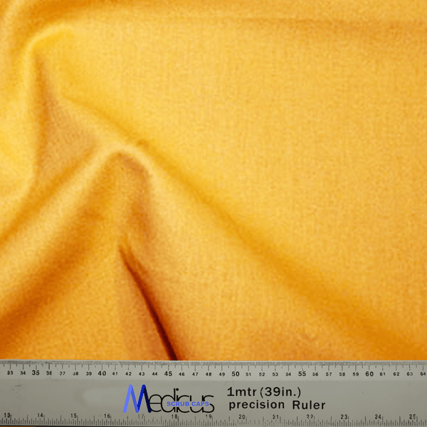 A Classic Plain Gold Yellow Scrub Cap from Medicus Scrub Caps drapes over a precise Medicare ruler, featuring durable design with clear measurements in centimeters and inches.