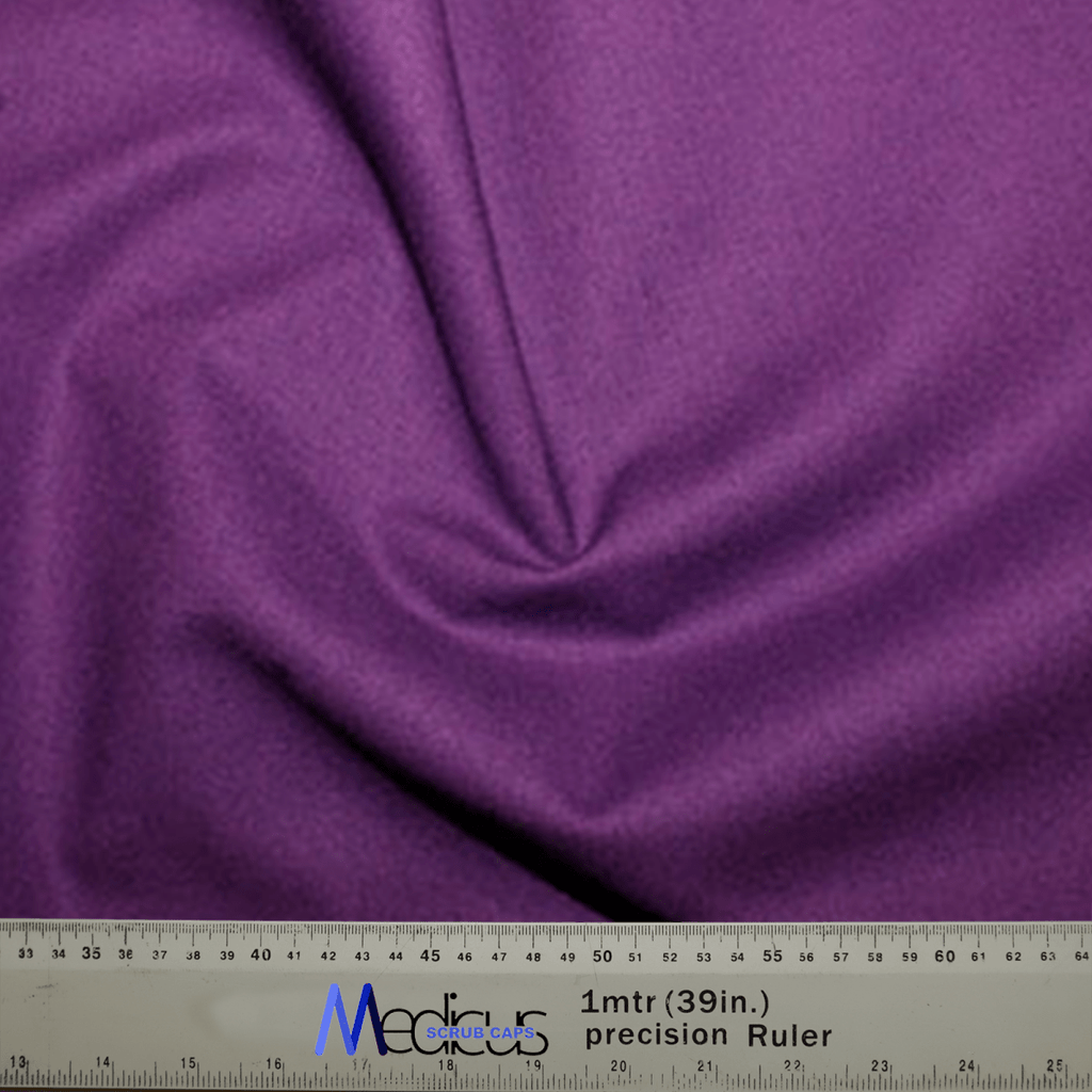 A folded Classic Plain Imperial Purple Scrub Cap by Medicus Scrub Caps is showcased, highlighting its comfort and durability, with a ruler at the bottom showing measurements in centimeters and inches.