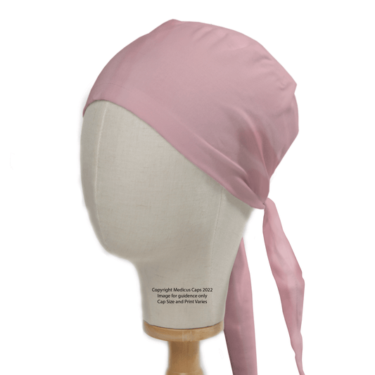 A mannequin head models a pale pink scrub cap with a long tail by Medicus Scrub Caps, ideal for healthcare professionals. The fabric is smooth and slightly shiny. Copyright 2022. Image for guidance only. Cap size and print may vary. Bulk discounts available.