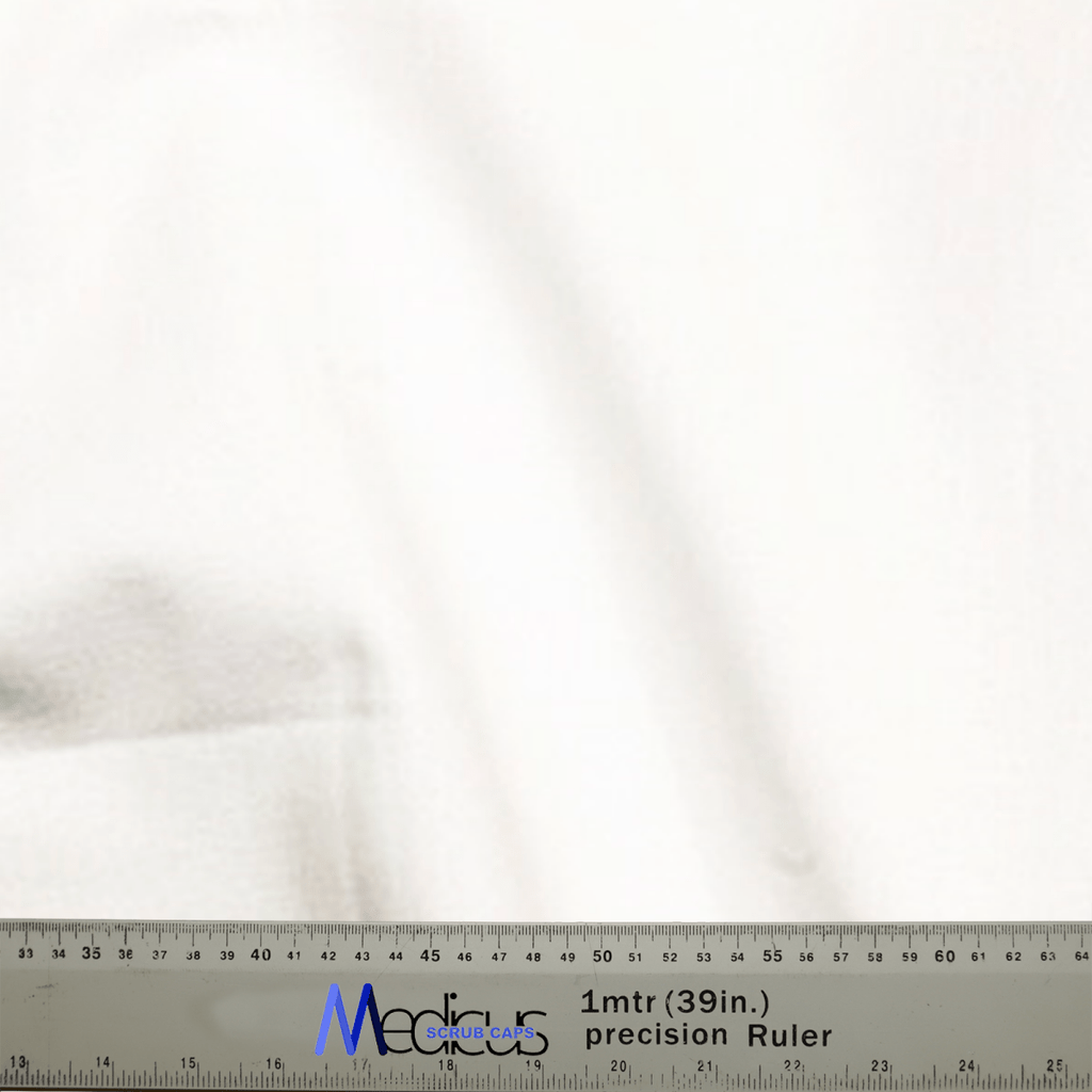 Close-up of a smooth, subtly folded white 100% cotton fabric by Medicus Scrub Caps. A one-meter precision ruler marked with centimeters and inches lies at the bottom. Ideal for crafting a Classic Plain White Scrub Cap or Theatre Hat.