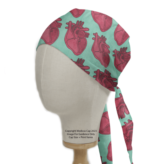 A mannequin head displays a teal Cross Section Heart Scrub Cap with red anatomical hearts. Perfect for healthcare professionals, it features long back ties and the note: “© Medicus Cap 2023, Image For Guidance Only, Cap Size & Print Varies.”.