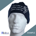 A mannequin head displays a Custom Scrub Cap by Medicus Scrub Caps featuring embroidery: This is what an awesome colorectal surgeon looks like with a hand point symbol. The background is diagonally split in light and dark green, with logos at the corners.