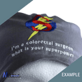 A custom gray scrub cap made from high-quality fabric by Medicus Scrub Caps displays an embroidered stylized ‘S’ with a lightning bolt and the text, Im a colorectal surgeon, what is your superpower? The cap is personalized with the “Medicus” logo and “EXAMPLE” in the corner.