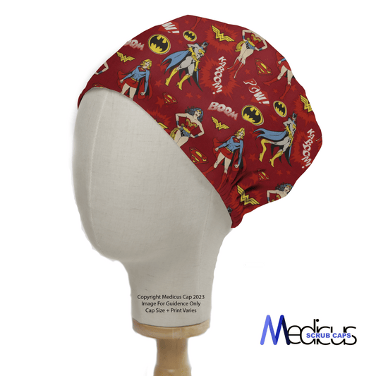 The Medicus Scrub Caps DC Comic Super Women Heroes On Red Scrub Cap showcases dynamic poses and action words like Boom! against a mannequin head on a white background.