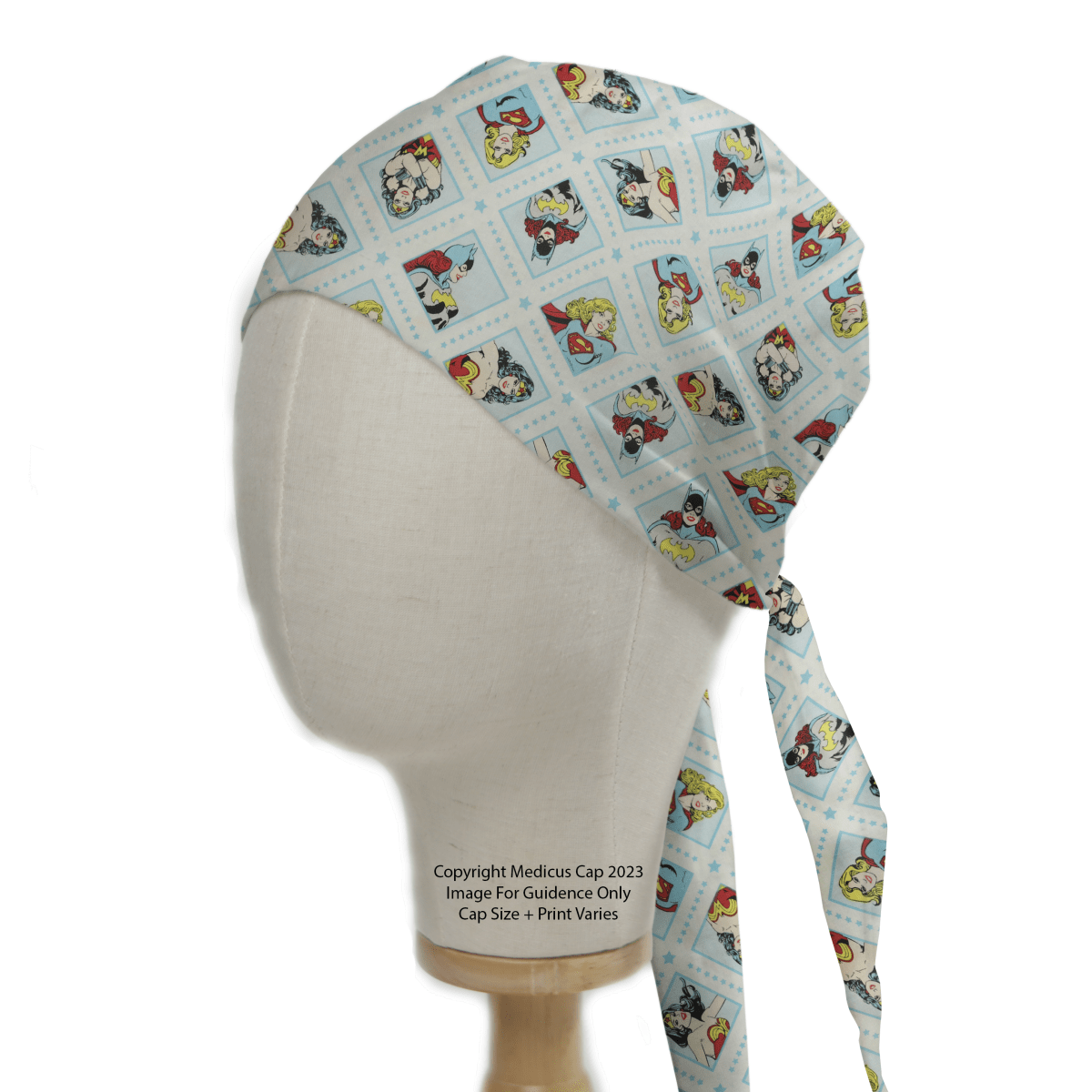 A mannequin head sports the DC Comic Super Women Superheroes Scrub Cap by Medicus Scrub Caps, featuring a vibrant light blue background with comic-style character illustrations in square frames for a playful design.