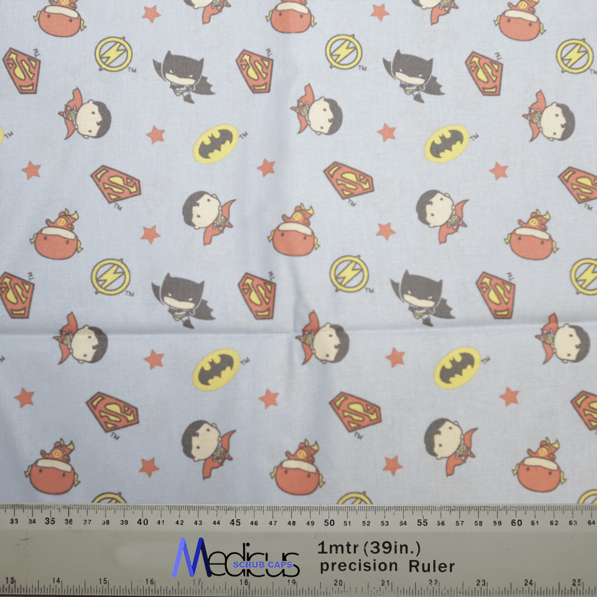 The Medicus Scrub Caps DC Kawaii Batman and Wonder Woman on Blue scrub cap features superhero symbols and characters like Batmans bat emblem, an S shield, a lightning bolt circle, and cute masked figures. Perfect for Wonder Woman fans. A ruler shows measurements in cm and inches.