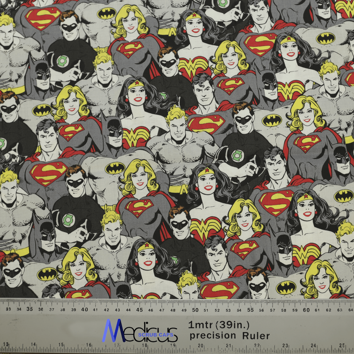 The DC Superheroes Monochrome Superman Superwoman Scrub Cap by Medicus Scrub Caps features classic comic heroes with S shields, capes, and lightning bolts. Ruler for scale.