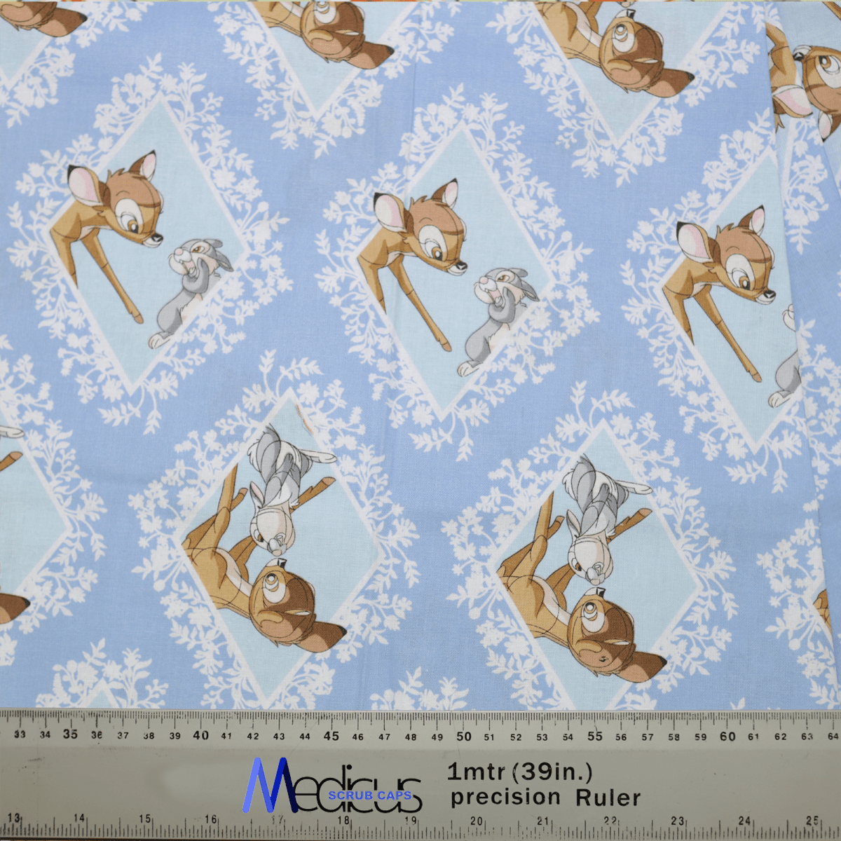 The Disney Bambi Thumper Blue Diamond Scrub Cap by Medicus features a pattern of Bambi and Thumper in diamond shapes on blue, with a 1-meter ruler for scale—ideal for healthcare professionals seeking charming attire.