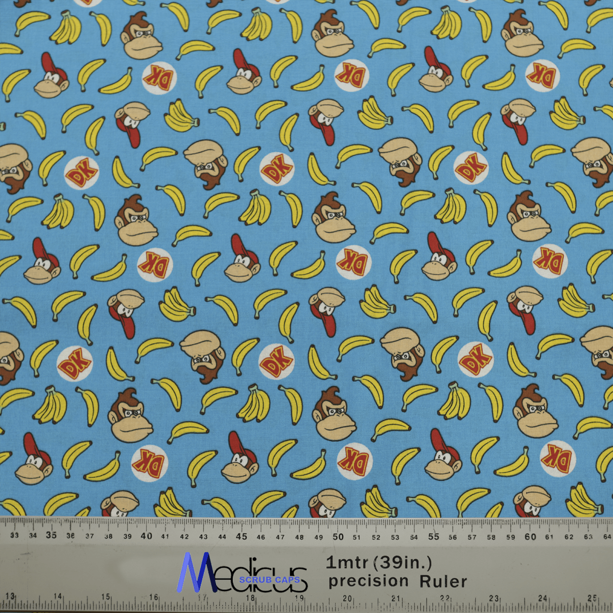 The DK Donkey Kong Bananas Blue Scrub Cap by Medicus Scrub Caps features playful gorilla characters, bananas, and DK logos on light blue fabric with measurement markings.