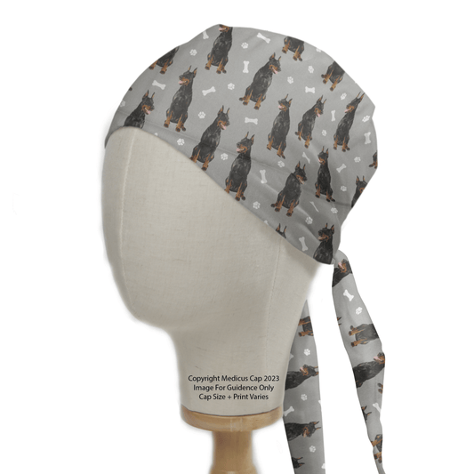 The Dobermann Dogs Grey Scrub Cap by Medicus Scrub Caps, showcased on a mannequin head, features an energetic pattern of Dobermanns, paw prints, and bones—ideal for healthcare professionals who love dogs.