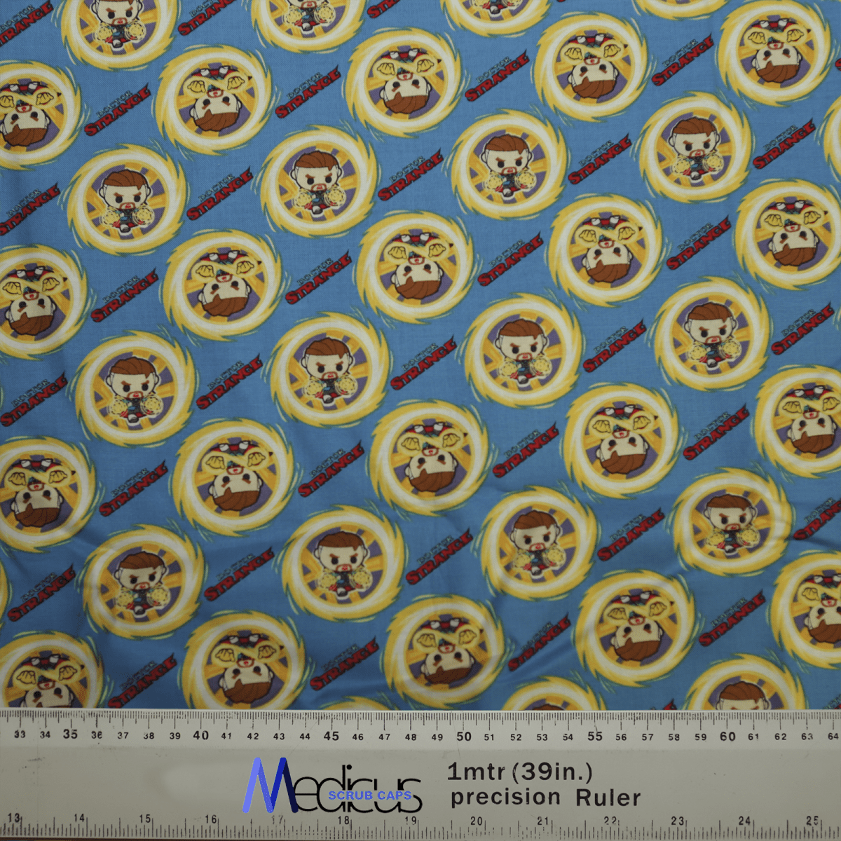 The Medicus Scrub Caps Doctor Strange Kawaii Superhero Scrub Cap exhibits cartoon characters in circular patterns on blue, with small, repeating figures of a character in a brown outfit with a distinctive hat and yellow ring. A ruler at the bottom shows size reference.